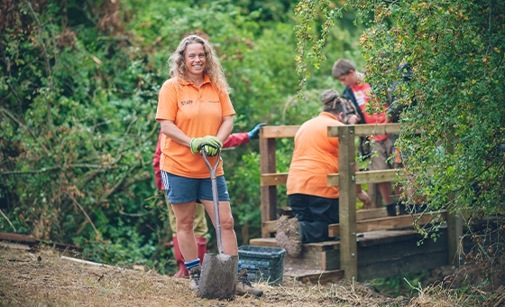 Staff member from charity seeds 4 success stood holding a spade and smiling